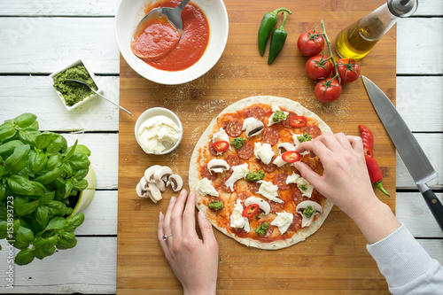 Traditional Italian pizza dough flat bread making tomato sauce mozzarella cheese salami prosciutto ham sausage basil hands chef wooden board kitchen preparation