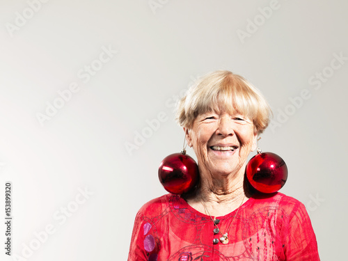 Senior woman wearing red baubles as earrings against white background