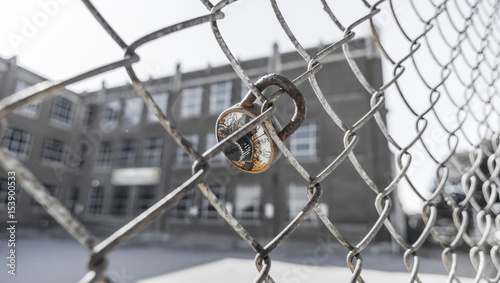 Rusty and broken combination lock attached to chain link fence outside of large urban school