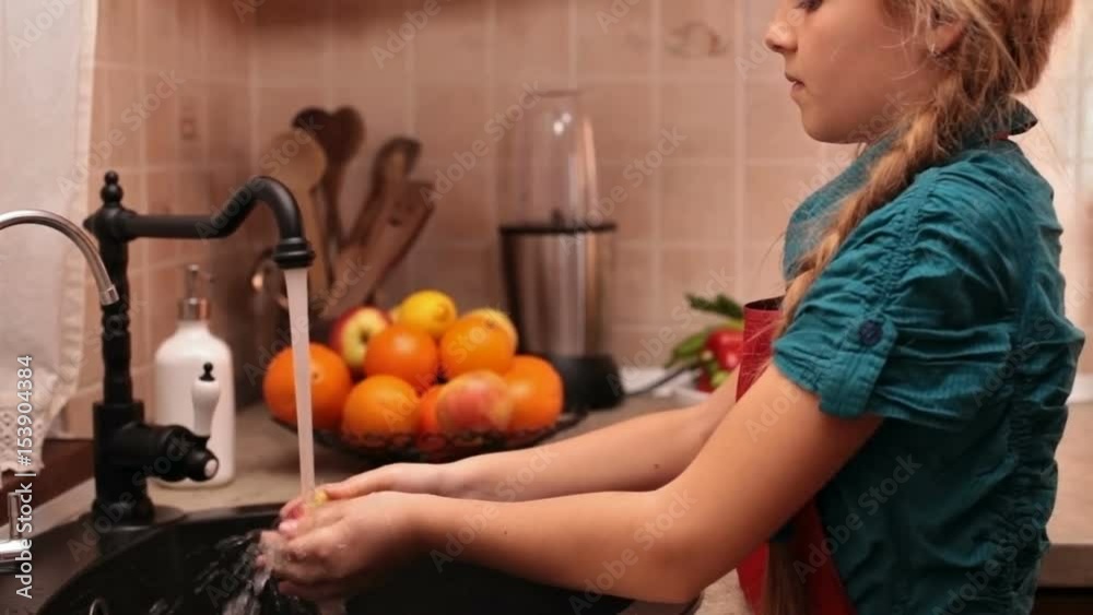 Little girl washing an apple at the kitchen sink - taking a bite of the fruit, camera tilts up from hands to face Little girl washing an apple at the kitchen sink - taking a bite of the fruit, camera tilts up from hands to face