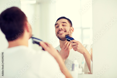 man shaving beard with trimmer at bathroom