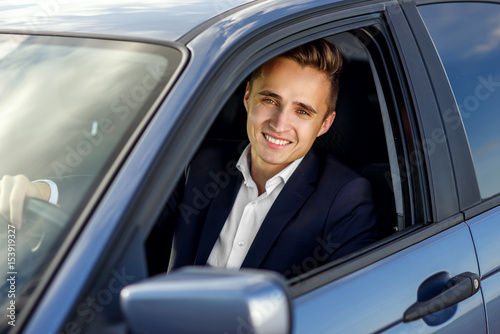 Attractive handsome smiling man in a business suit driving an expensive car