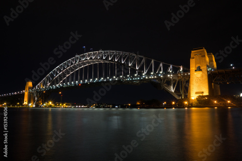 Long exposure night shot of the city center skyline of Sydney looking over the harbor bridge. Strong reflection on the water.