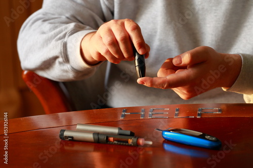 Diabetes. Blood glucose meter. Adult man measuring sugar level in blood at the table.