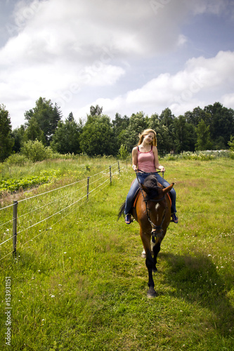 Portrait of young and beautiful woman riding on the horse on the field, cloudy summer day.