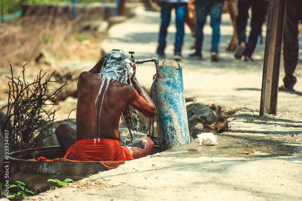 Sadhu is washed under running water near the road