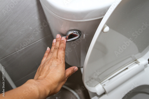 A woman hand pressing a white toilet bowl or flush toilet in the bathroom.  photo