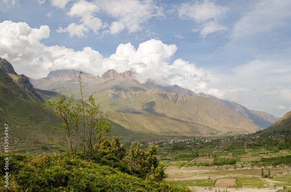 Naklejka premium Mountain settlement in the Caucasus is located among the mountains in a quiet valley against the background of beautiful clouds