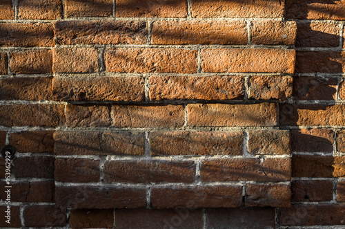 Old orange brick wall background texture. Front view. Sun light and shadows on brick wall.