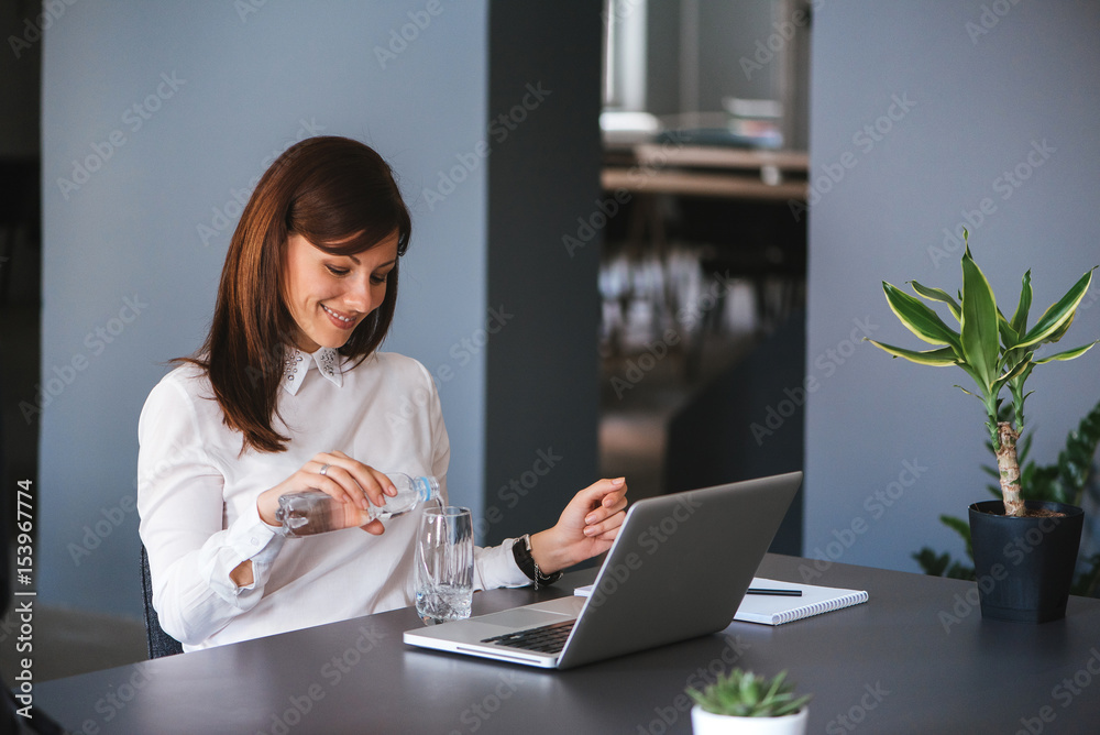 Portrait of happy businesswoman pouring water in glass from bottle at office Portrait of happy businesswoman pouring water in glass from bottle at office