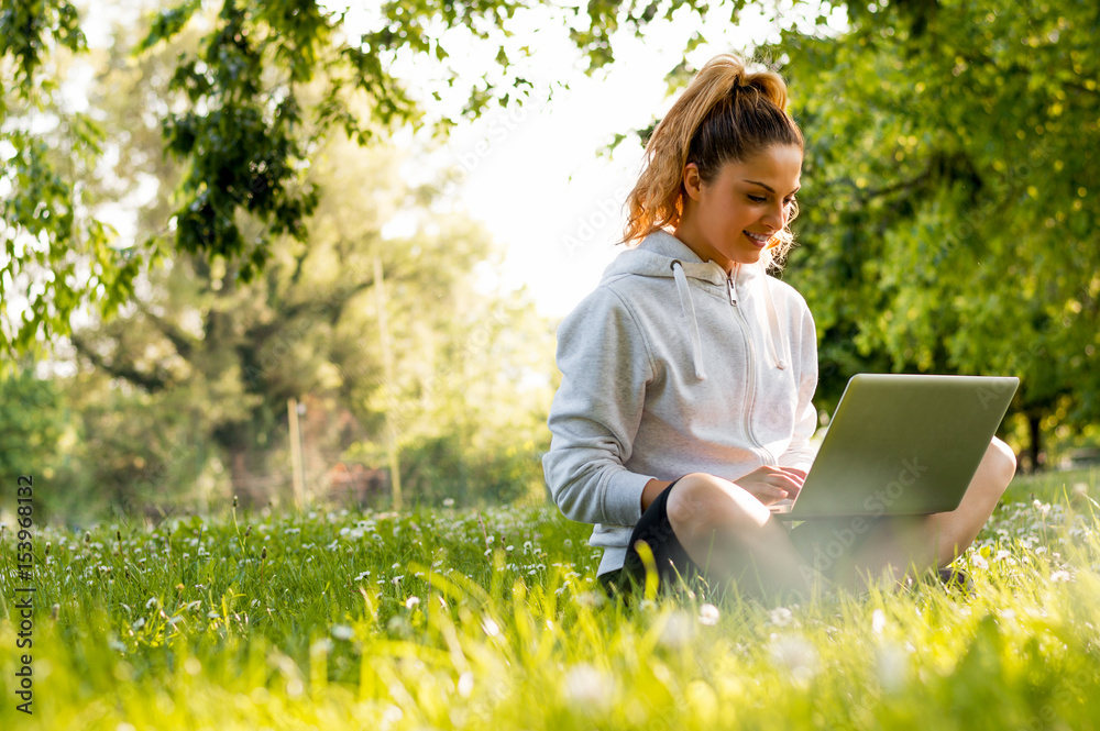 Charming young woman is working on laptop while sitting on grass Charming young woman is working on laptop while sitting on grass
