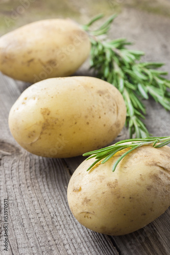  Fresh rosemary and raw potatoes on wooden table