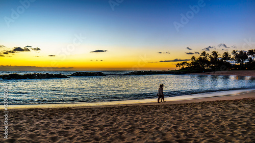 Couple strolling on the beach at sunset under blue sky on the West Coast of the Hawaiian island of Oahu, with a few colorful clouds on the horizon photo