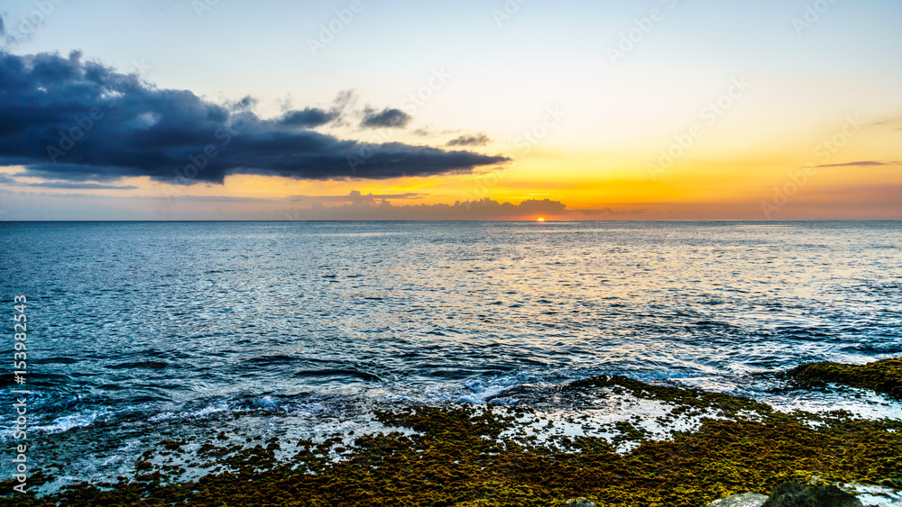 Sunset over the horizon with a few clouds and the rocky shores of the west coast of the tropical Hawaiian island of Oahu