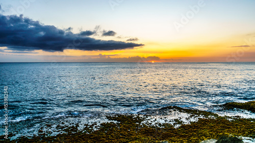 Sunset over the horizon with a few clouds and the rocky shores of the west coast of the tropical Hawaiian island of Oahu