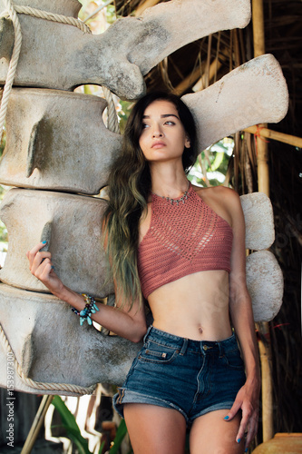 Portrait sexy brunette in top and jeans shorts against a background decorative photo