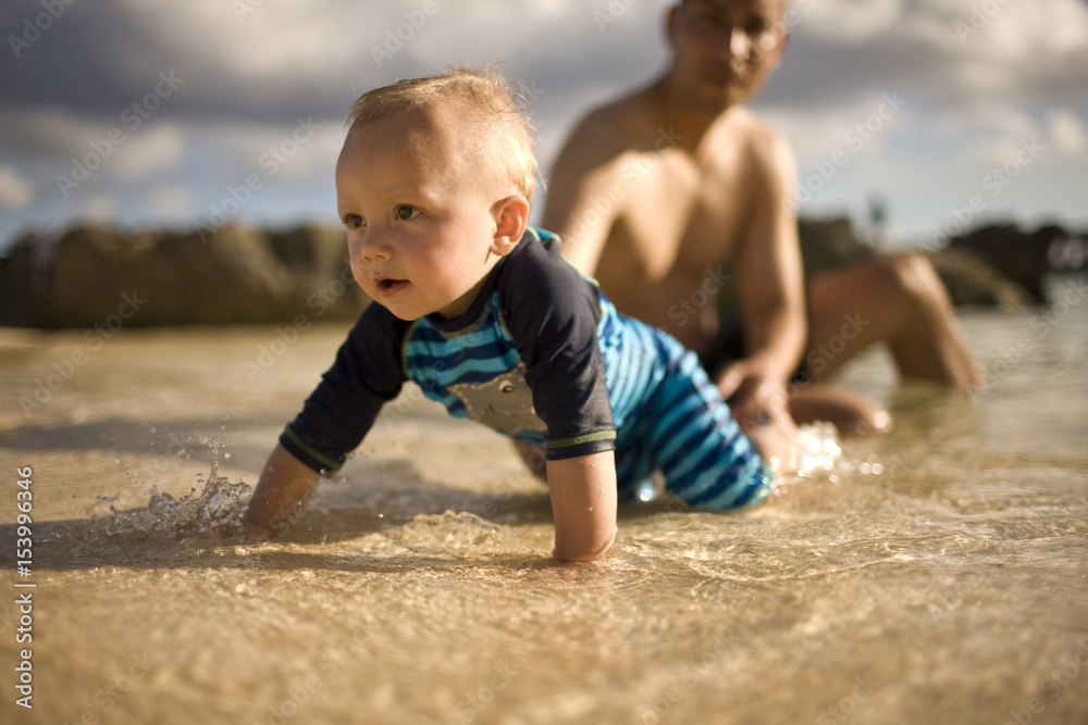 Baby crawling in water while father in background Baby crawling in water while father in background