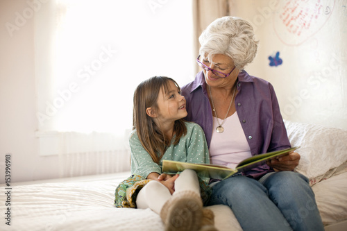 Grandmother reading a book for her granddaughter while sitting at home