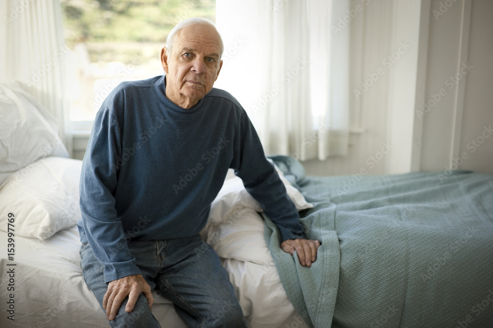 Portrait of a concerned senior man sitting on a bed in his bedroom. Portrait of a concerned senior man sitting on a bed in his bedroom.