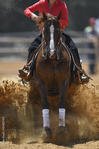 The front view of a rider in cowboy chaps and boots sliding the horse in the sand © PROMA
