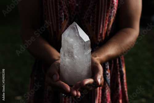 A young woman holding a large, luminous quartz crystal appears powerful in dramatic lighting. photo