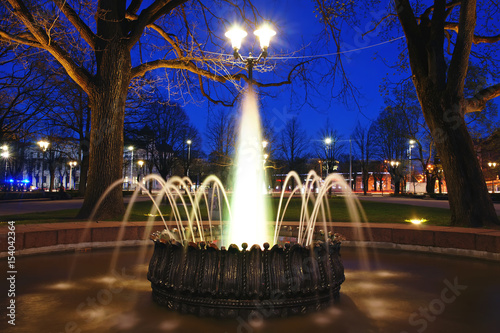 The white lighted fountain at night in the city park in spring