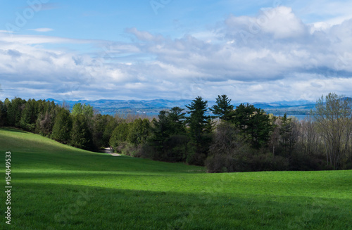 Fototapeta Naklejka Na Ścianę i Meble -  looking across farm field in shadows to Lake Champlain, Vermont , and beyond to mountains in New York state
