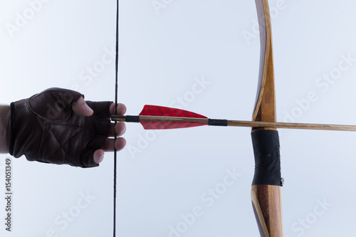Archer wearing open fingers leather gloves drawing a traditional english longbow with a red feather medieval arrow on it isolated on white background