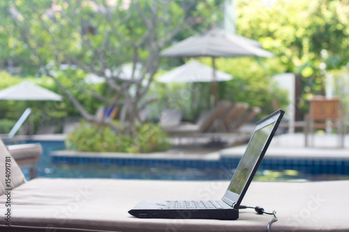 side view of laptop on the deckchair in swimming pool side. computer open in exterior yard for working outdoor. Luxury hotel background. select focus
