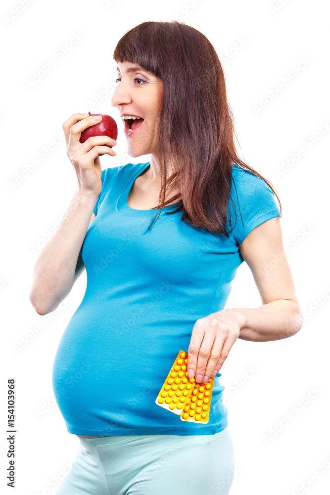 Happy pregnant woman eating fresh apple and holding medical pills or supplements, choice between healthy food and pills Happy pregnant woman eating fresh apple and holding medical pills or supplements, choice between healthy food and pills