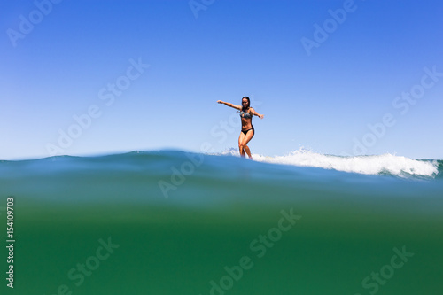 A young, healthy girl balances carefully as she cross-steps on a longboard over a vibrant, tropical sea in Australia.