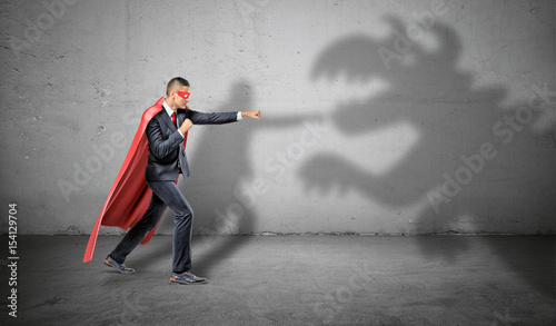 A superhero businessman fighting off a dragon shadow on concrete background.