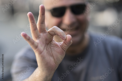 Caucasian man with sunglasses making ok sign at camera. Selective focus on foreground © cineberg