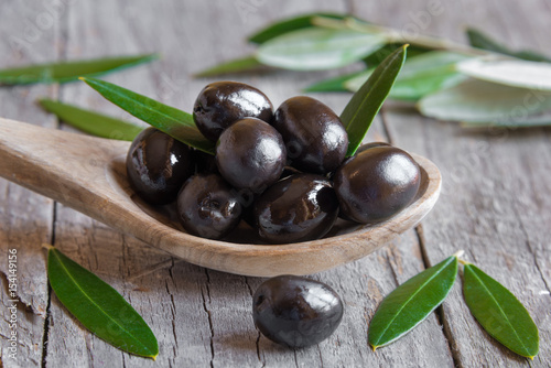 Obraz na płótnie Black olives on wooden spoon with leaves