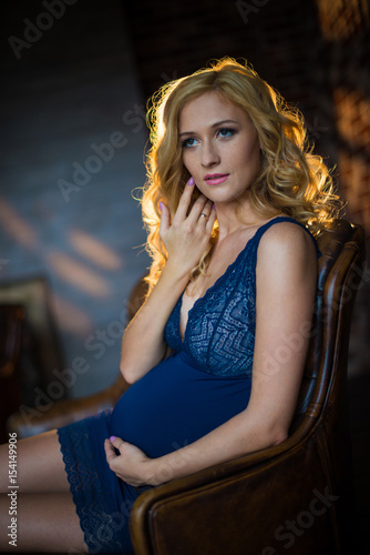 A beautiful pregnant girl is sitting on the couch in a loft interior.