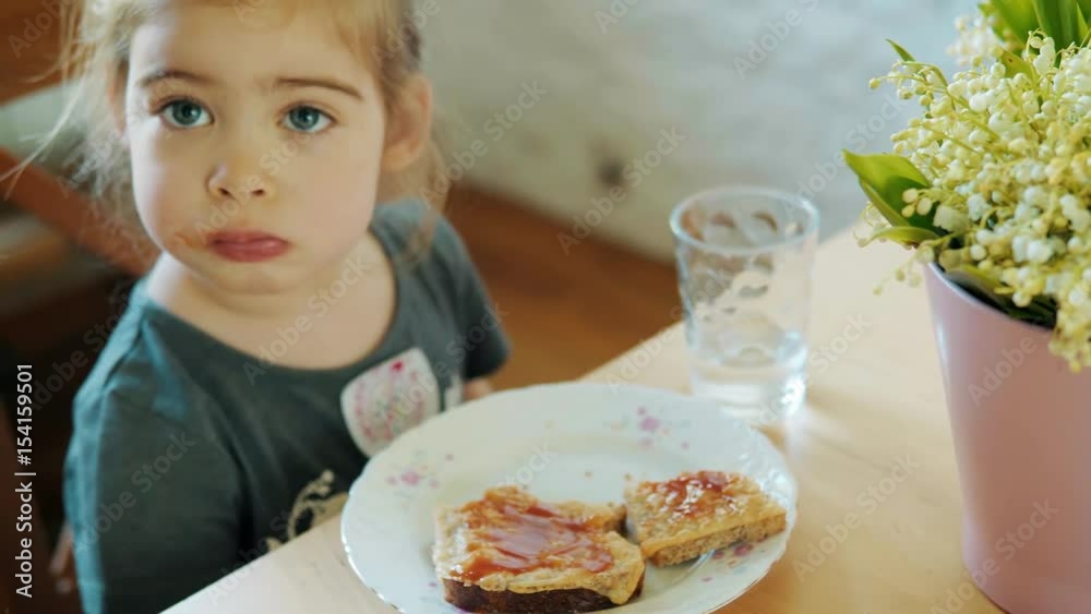 One small and cute girl eating breakfast at the table with a bouquet of flowers One small and cute girl eating breakfast at the table with a bouquet of flowers
