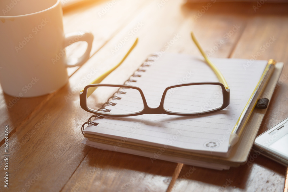 Notebook or note pad,smart phone,cup of coffee and glasses on wooden background with copy space. office desk concept Notebook or note pad,smart phone,cup of coffee and glasses on wooden background with copy space. office desk concept