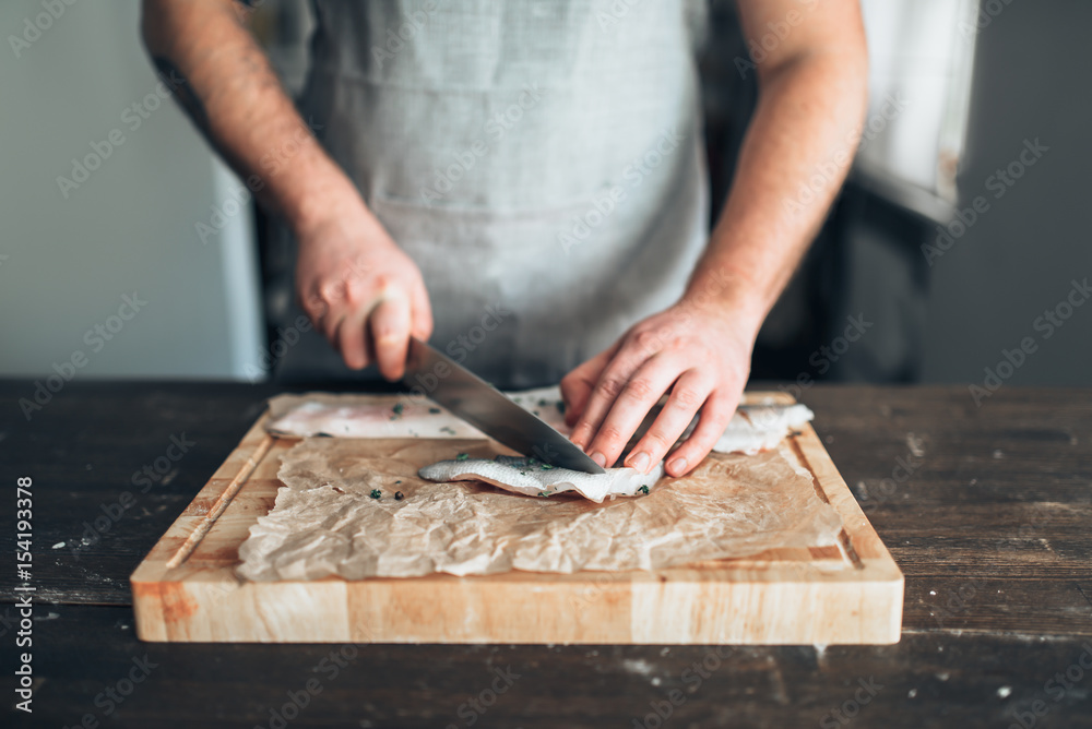 Chef cuts raw fish slices on wooden cutting board Chef cuts raw fish slices on wooden cutting board
