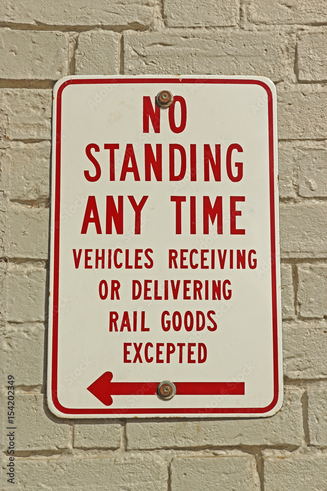 red and white No Standing Any Time sign on a painted white brick wall red and white No Standing Any Time sign on a painted white brick wall
