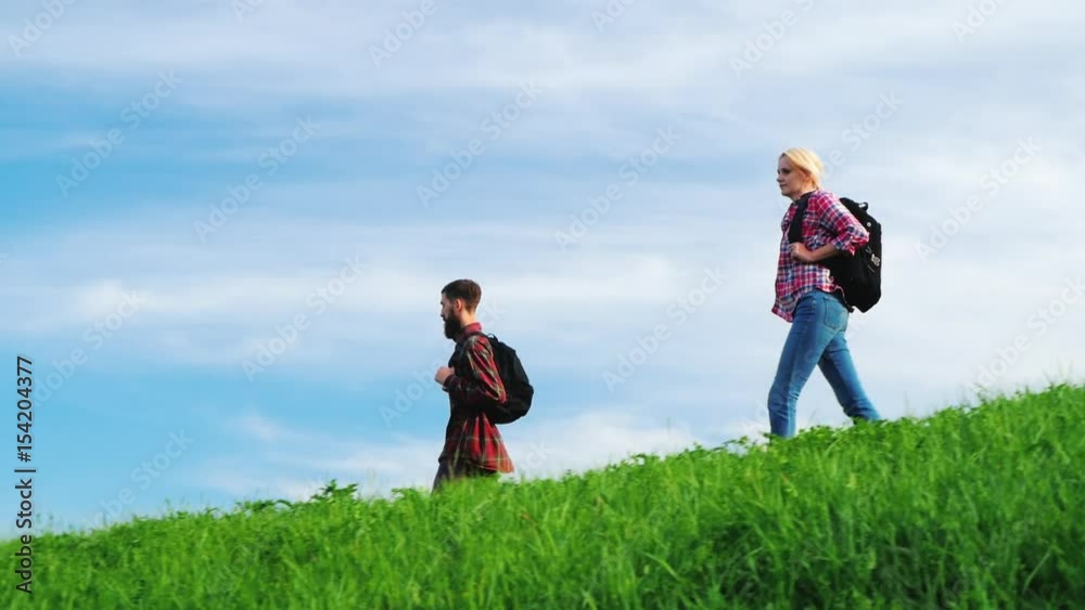 A couple of tourists with backpacks are walking along the crest of a large green hill. A couple of tourists with backpacks are walking along the crest of a large green hill.