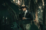 Senior explorer standing in dense jungle looking carefully.