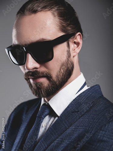 portrait of handsome fashion businessman  model dressed in elegant blue suit with sunglasses.posing on gray background in studio photo