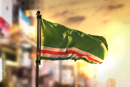 Chechen Republic of Ichkeria Flag Against City Blurred Background At Sunrise Backlight