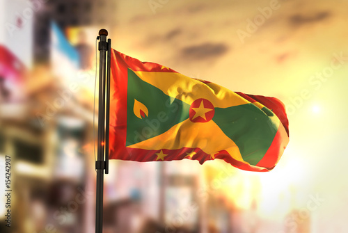 Grenada Flag Against City Blurred Background At Sunrise Backlight