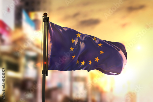 European Flag Against City Blurred Background At Sunrise Backlight