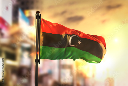 Libya Flag Against City Blurred Background At Sunrise Backlight