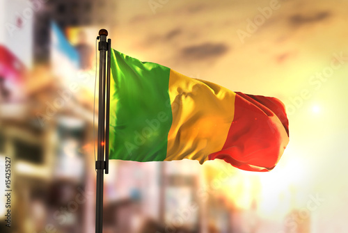 Mali Flag Against City Blurred Background At Sunrise Backlight
