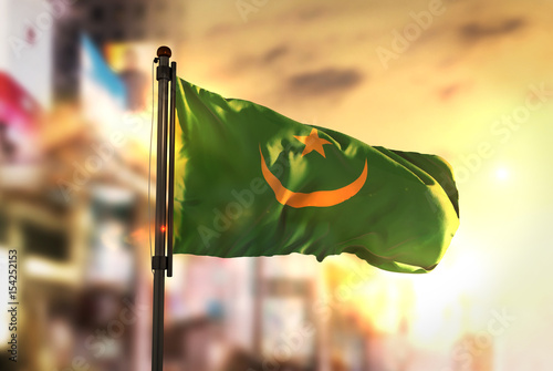 Mauritania Flag Against City Blurred Background At Sunrise Backlight