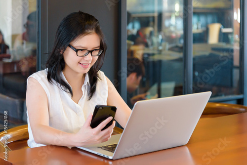 Asian charming beautiful girl freelancer in casual suit working or check information from website on her laptop and smartphone or mobile phone in coffee shop or modern office. Business Concept.