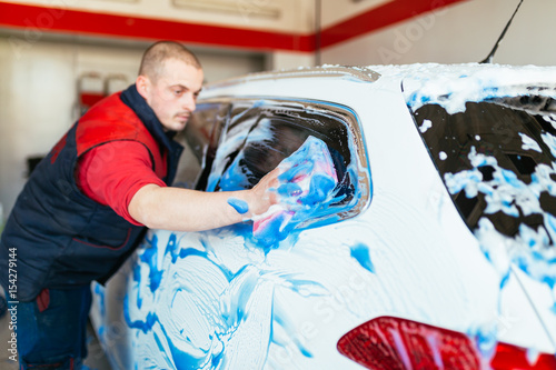 A man cleaning car with sponge using blue foam, car detailing (or valeting) concept. Selective focus. 